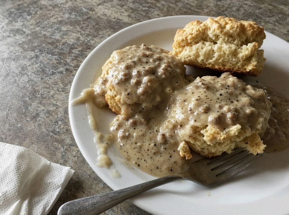 Biscuits smothered in peppery sausage gravy on a white plate, with a fork